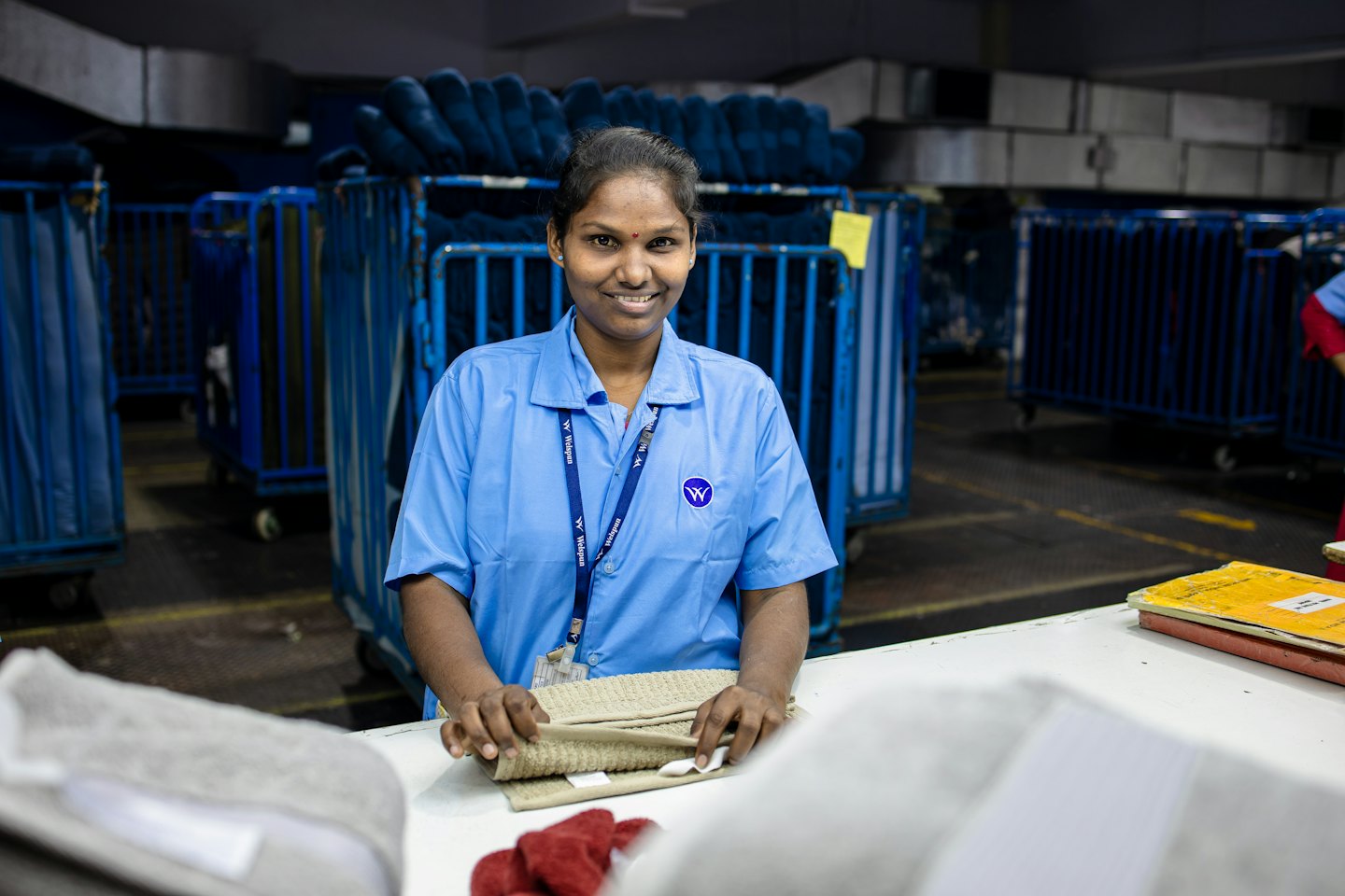 Woman folds beige fabric on a workstation in a textile factory.