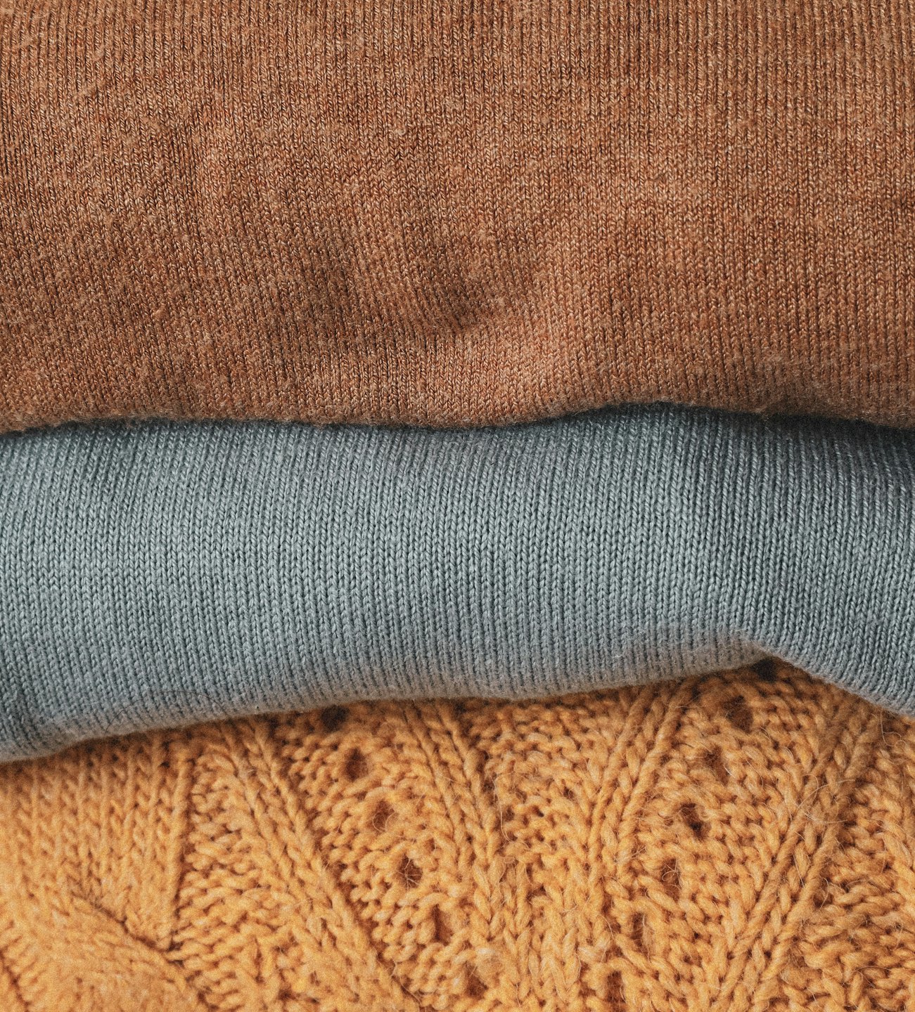 Three folded sweaters stacked neatly on a shelf.